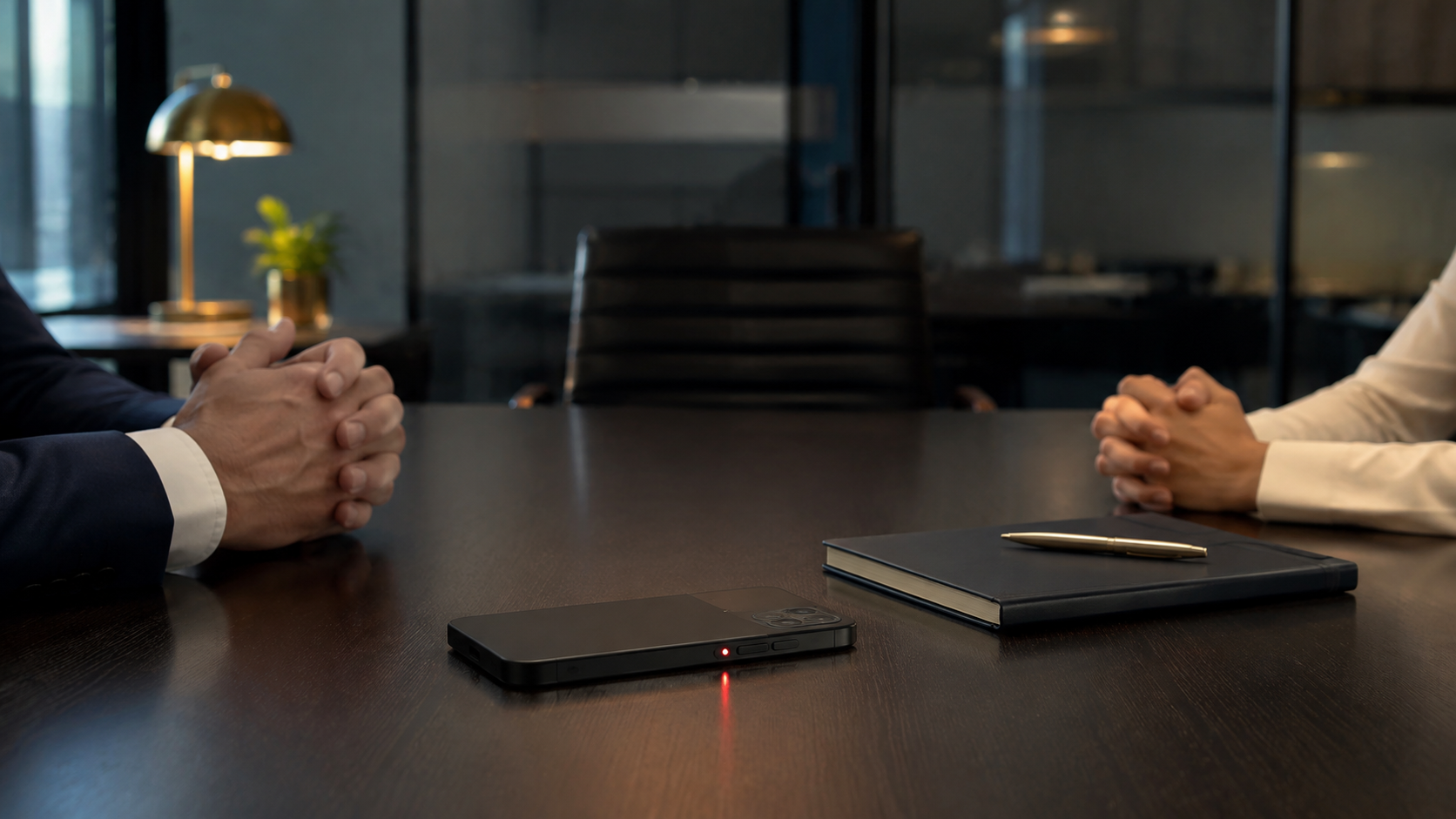 Two coworkers in a modern open-plan office speaking privately near a window, with a smartphone face-down on a desk in the foreground